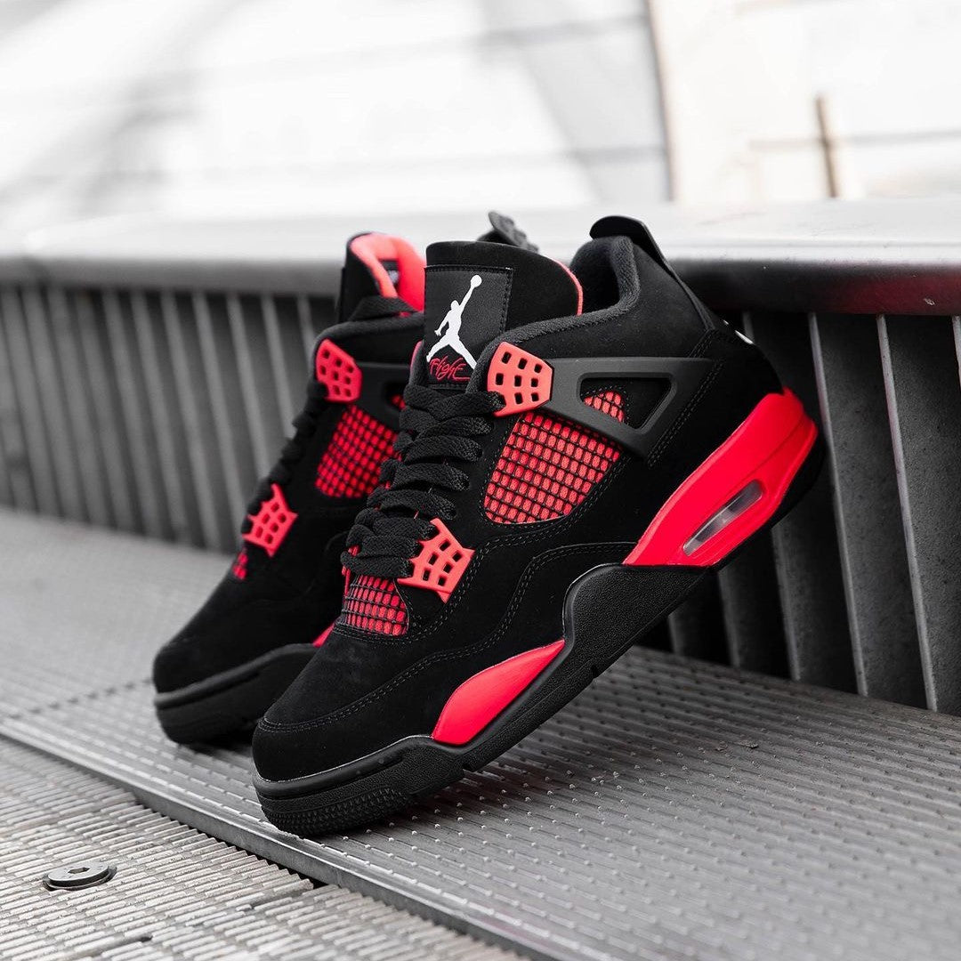 Black and red Air Jordan 4 sneakers displayed on a textured surface, showcasing their stylish design and vibrant colors.