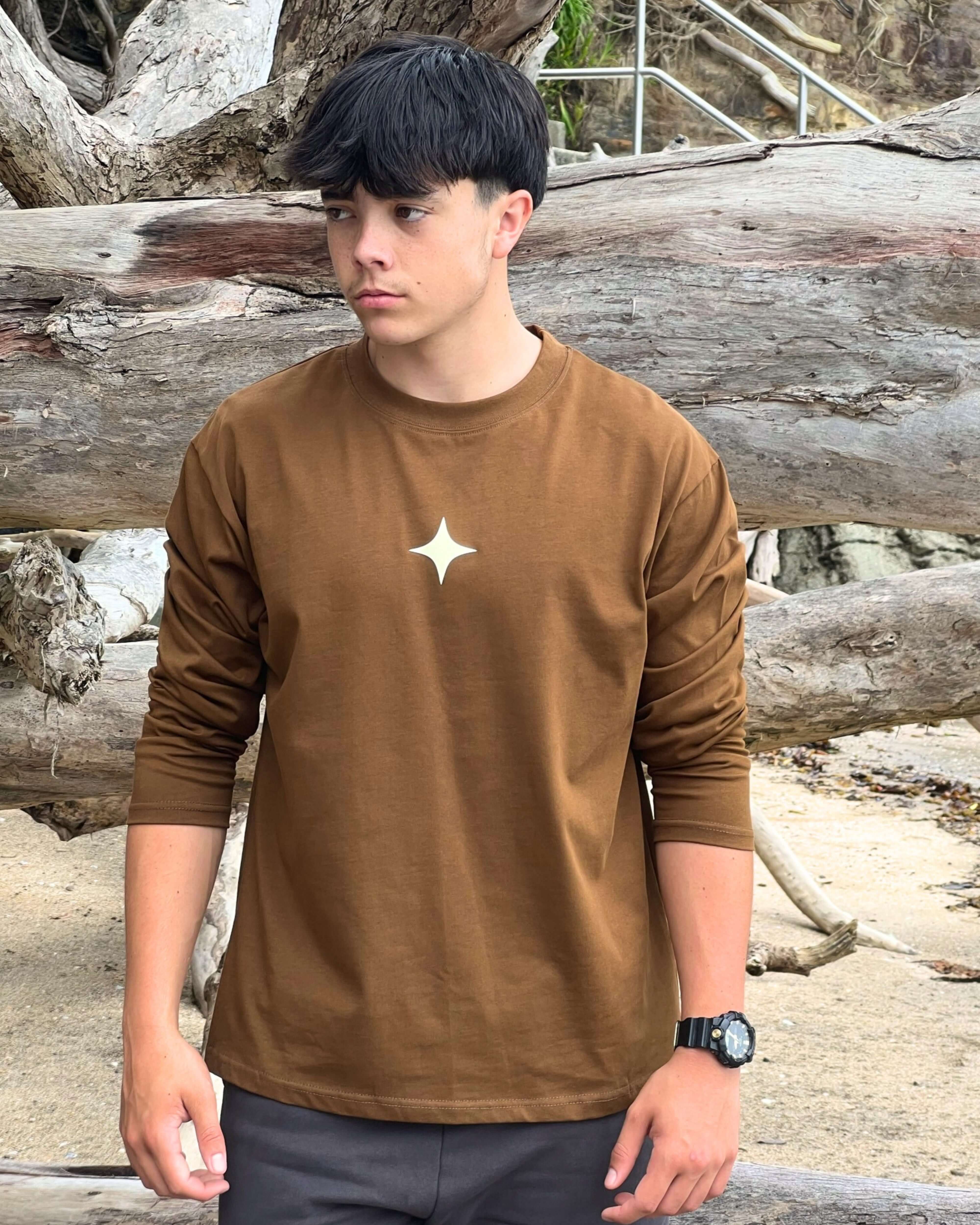 Model wearing a mocha long sleeve tee with star design against a natural outdoor backdrop.