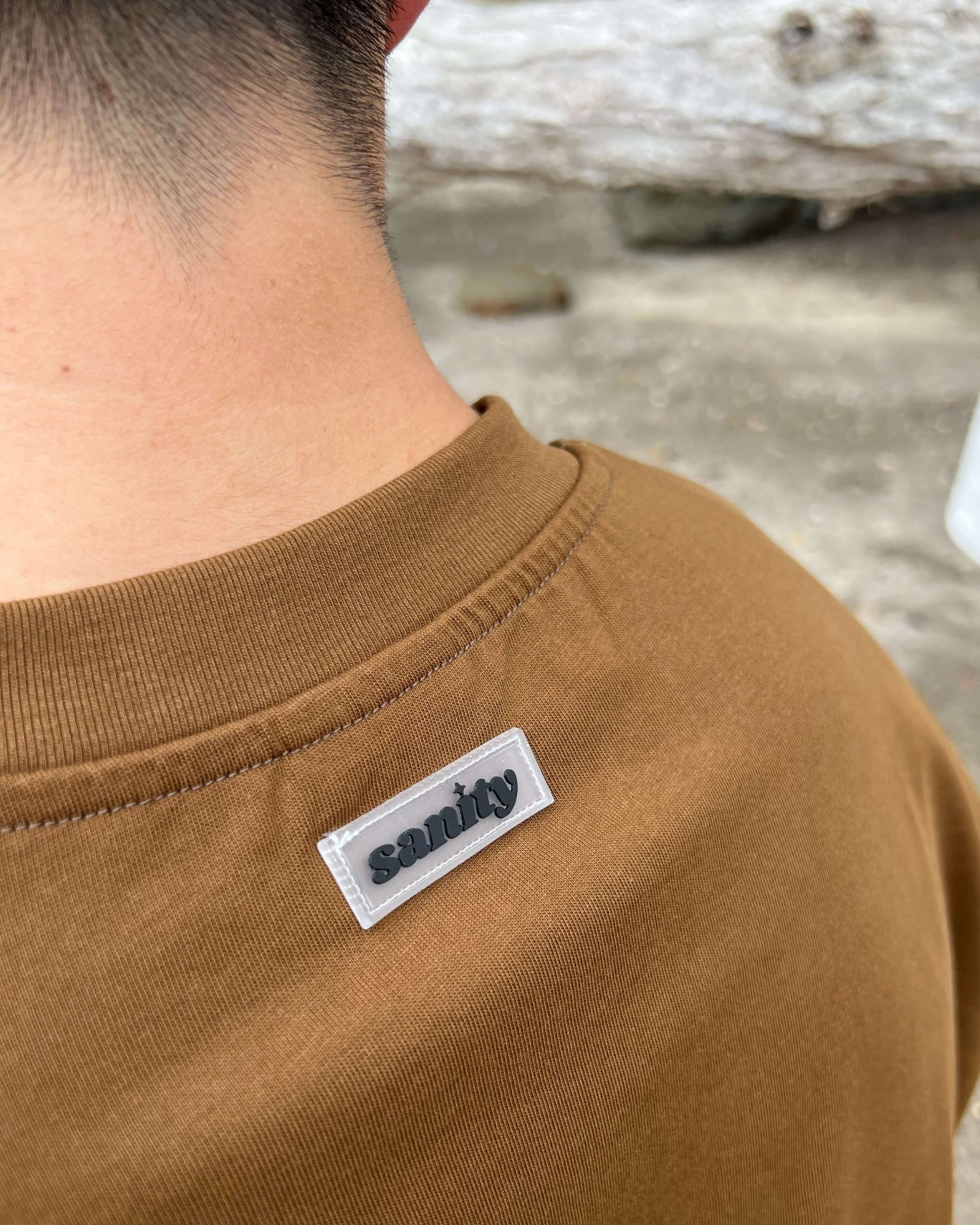 Close-up of Sanity Mocha Long Sleeve Tee label on the back, showcasing quality craftsmanship and design.