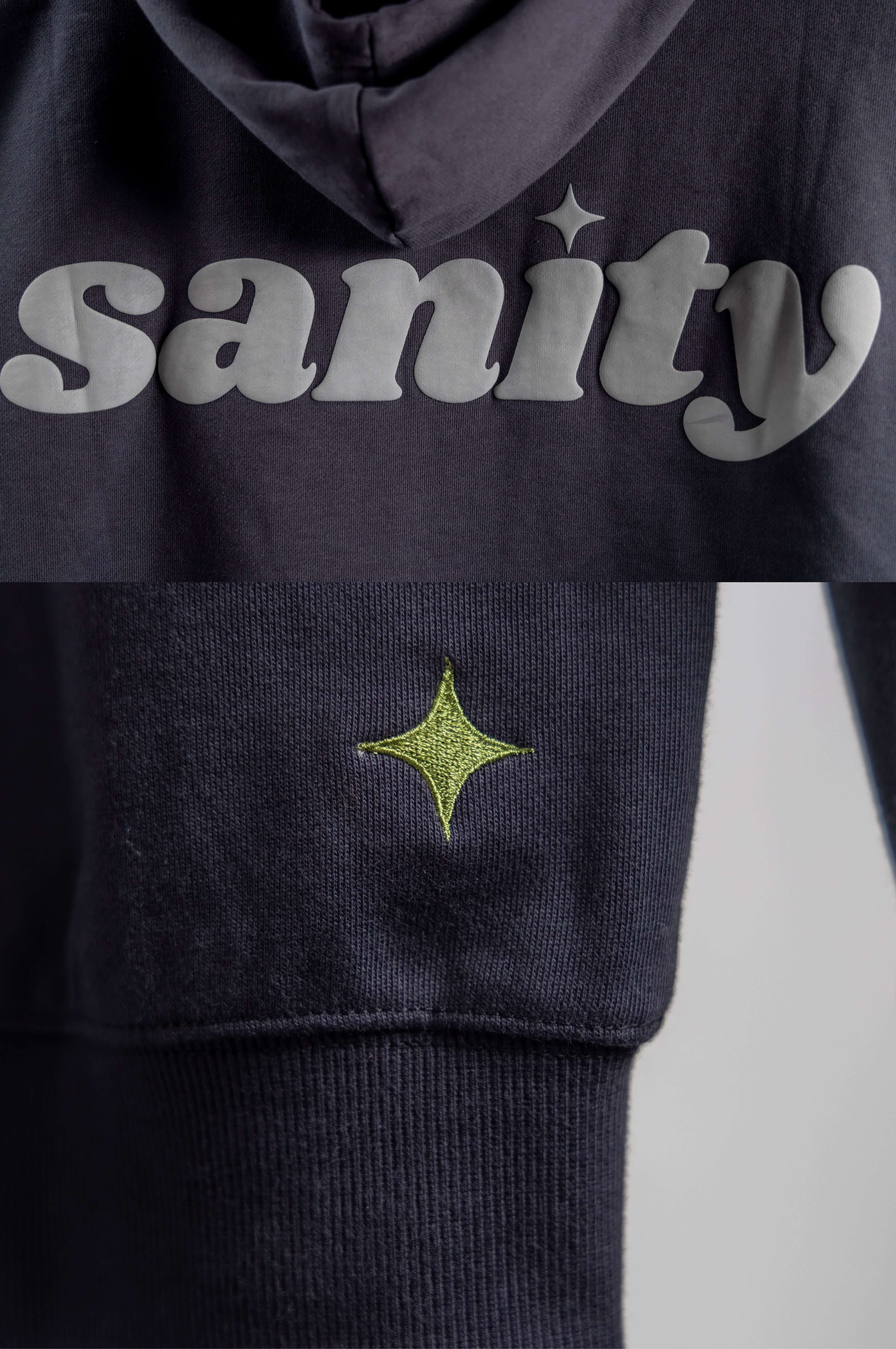Close-up of Sanity hoodie featuring grey puff print and green star embroidery on midnight black fabric.