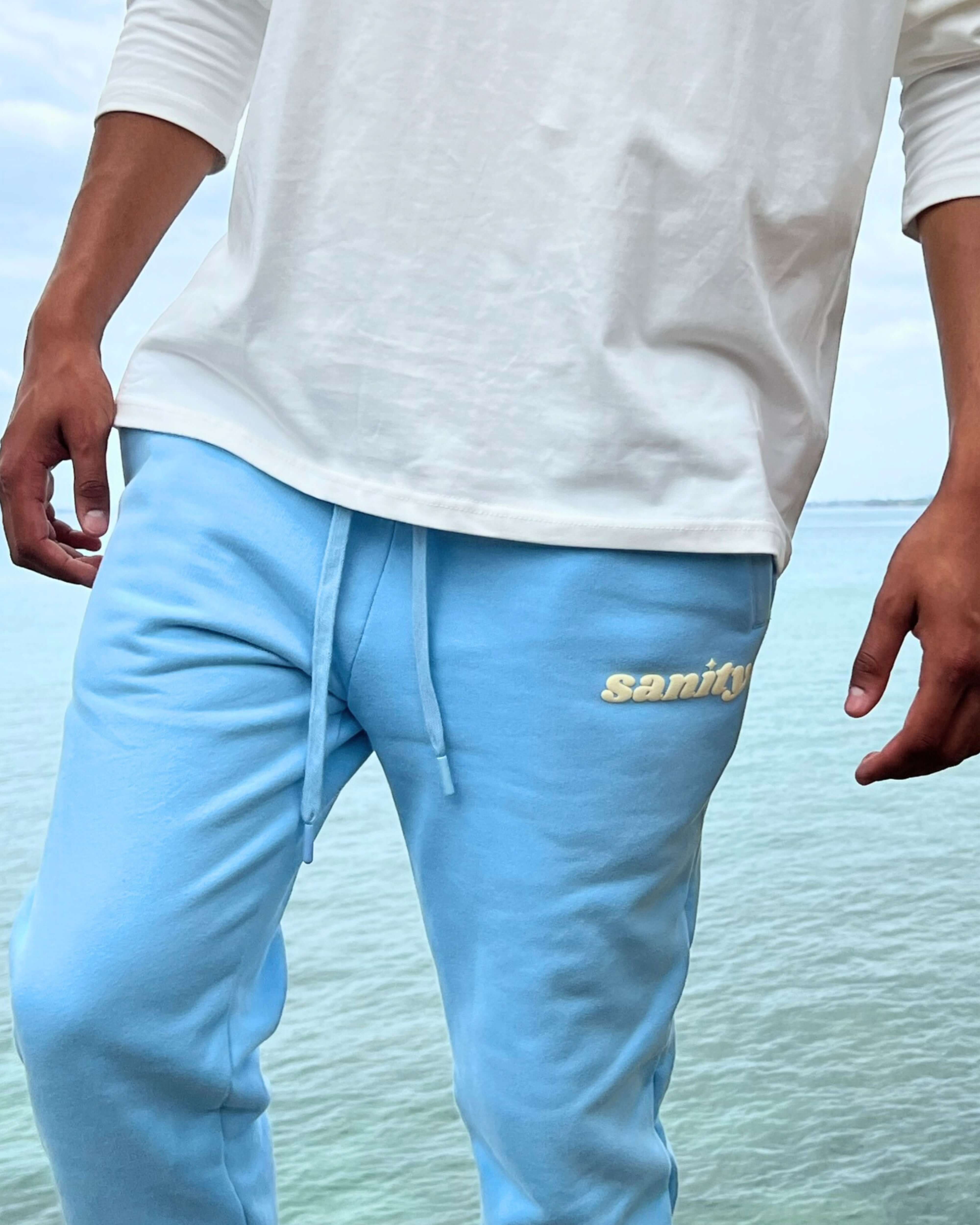 Man wearing Sanity Ice Blue Trackpants by the water, showcasing comfort and stylish casual wear.