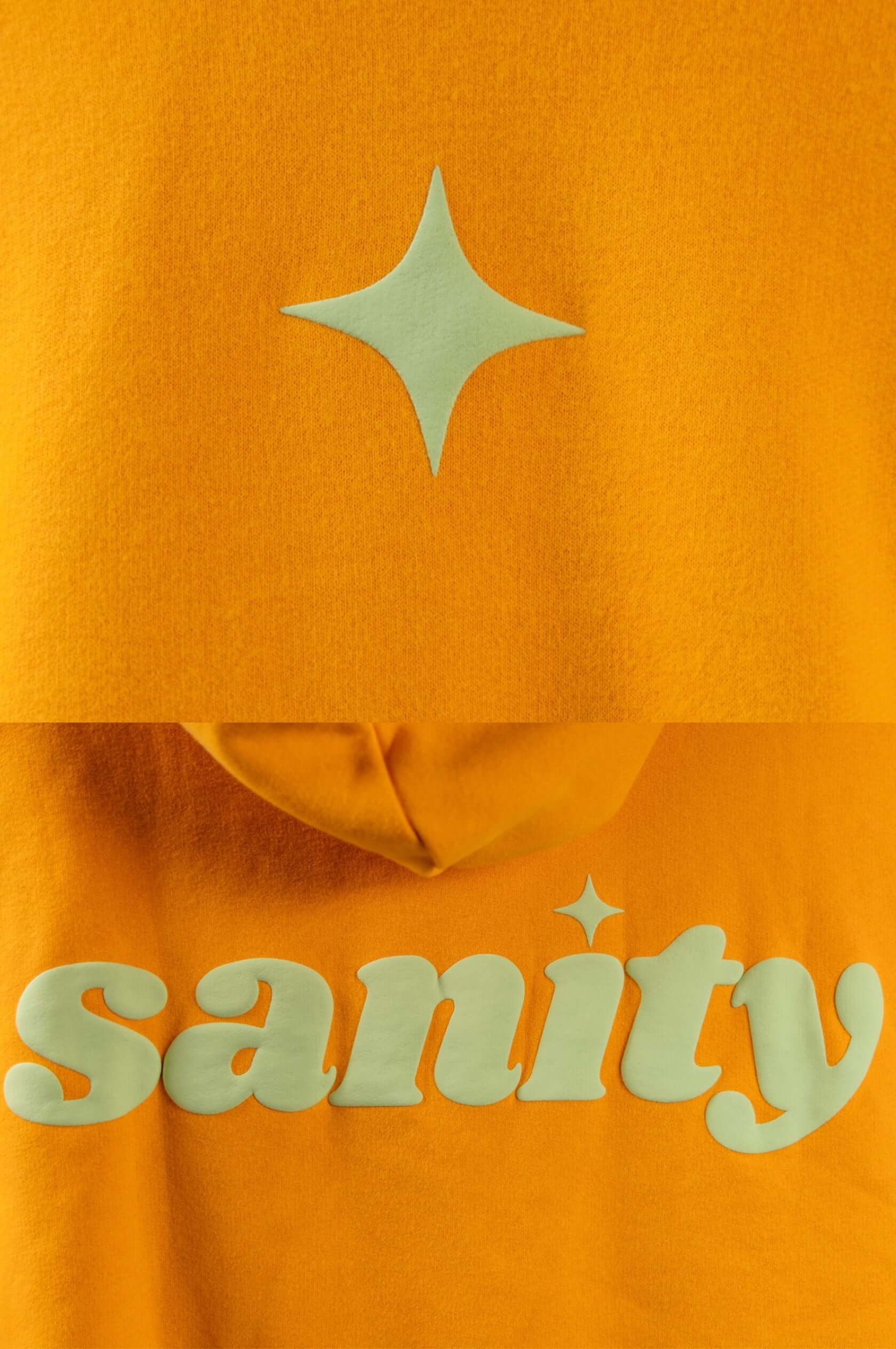 Detail of Sanity clothing logo on an orange hoodie with mint green embroidery and star accent.