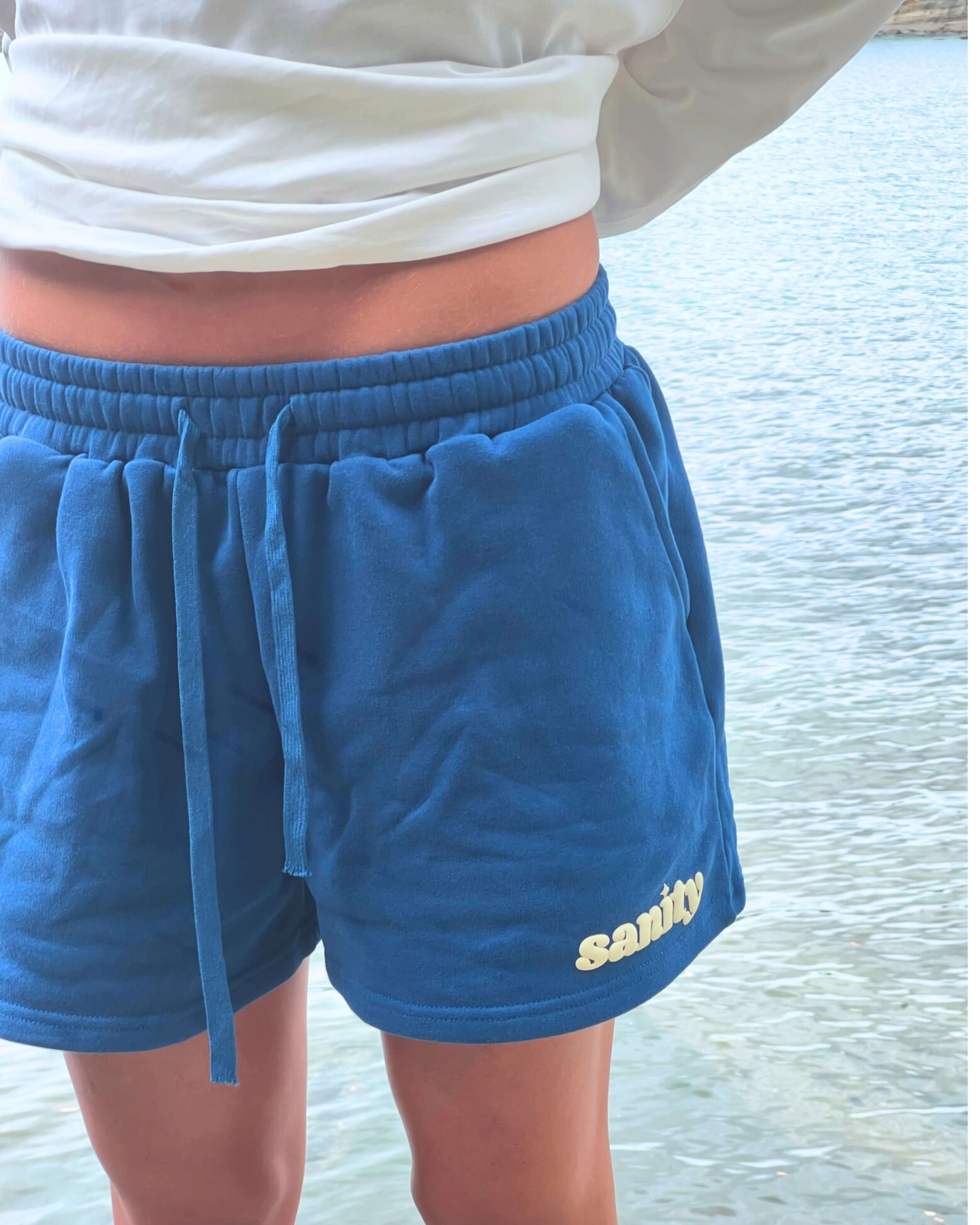 Sanity Deep Sea Women's Shorts in deep navy near water, featuring drawcord and logo design for comfort and style.
