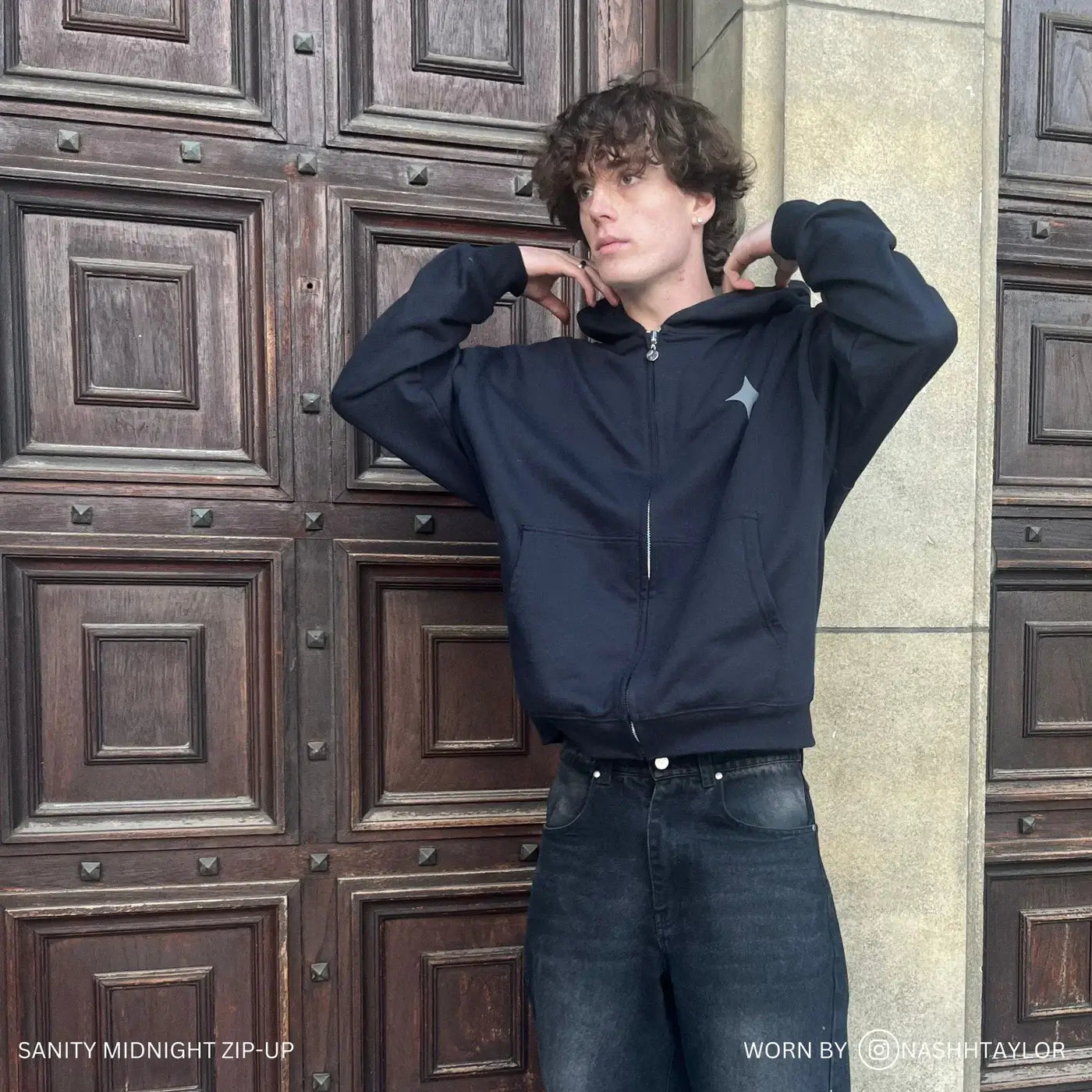 Model wearing Sanity Midnight Zip-Up hoodie, showcasing its comfort and style against a rustic backdrop.