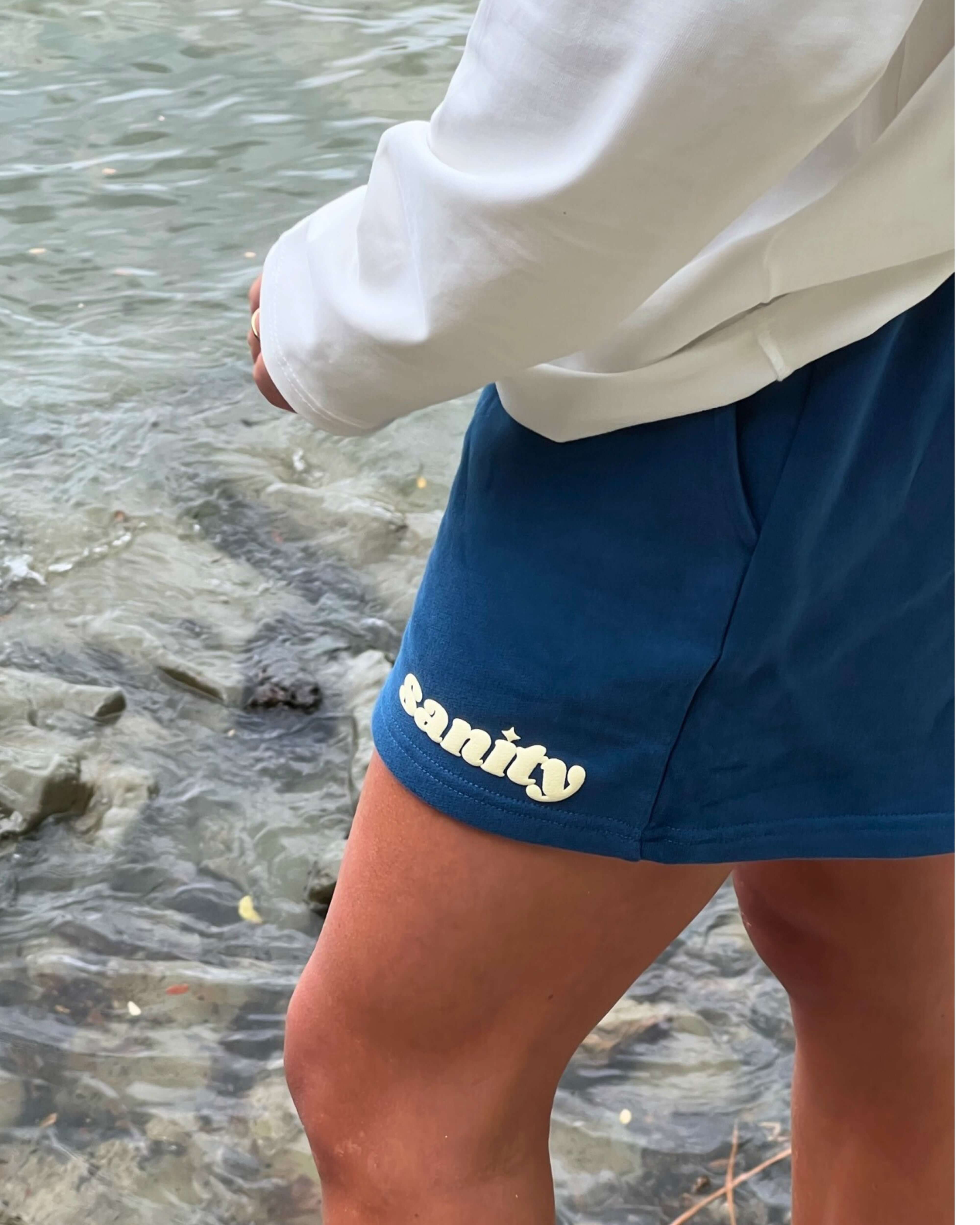 Model wearing Sanity Deep Sea women's shorts by the water, showcasing the navy color and comfortable fit.