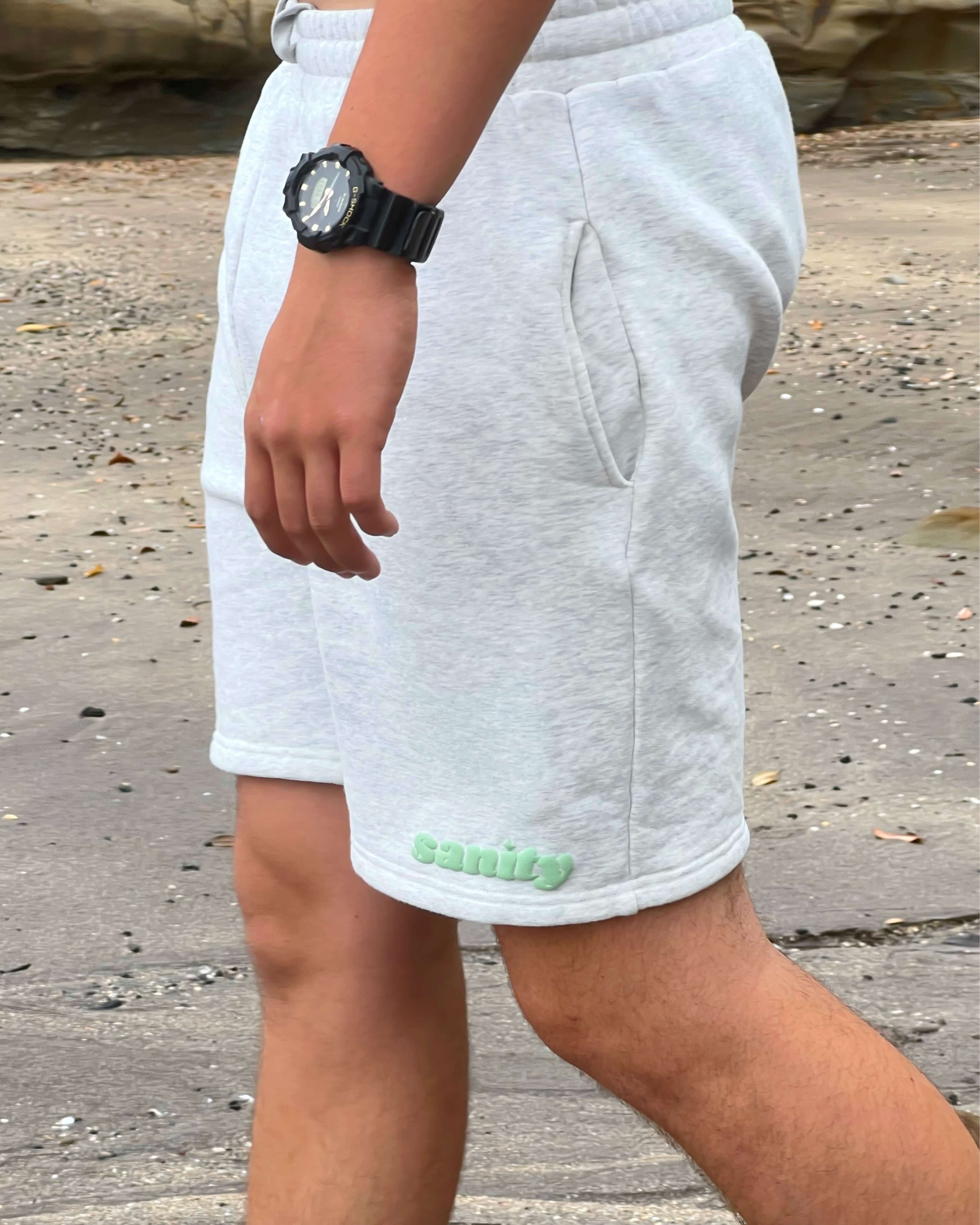 Man wearing Sanity gray shorts with side pockets, showcasing minimalist style and comfort on a sandy beach.