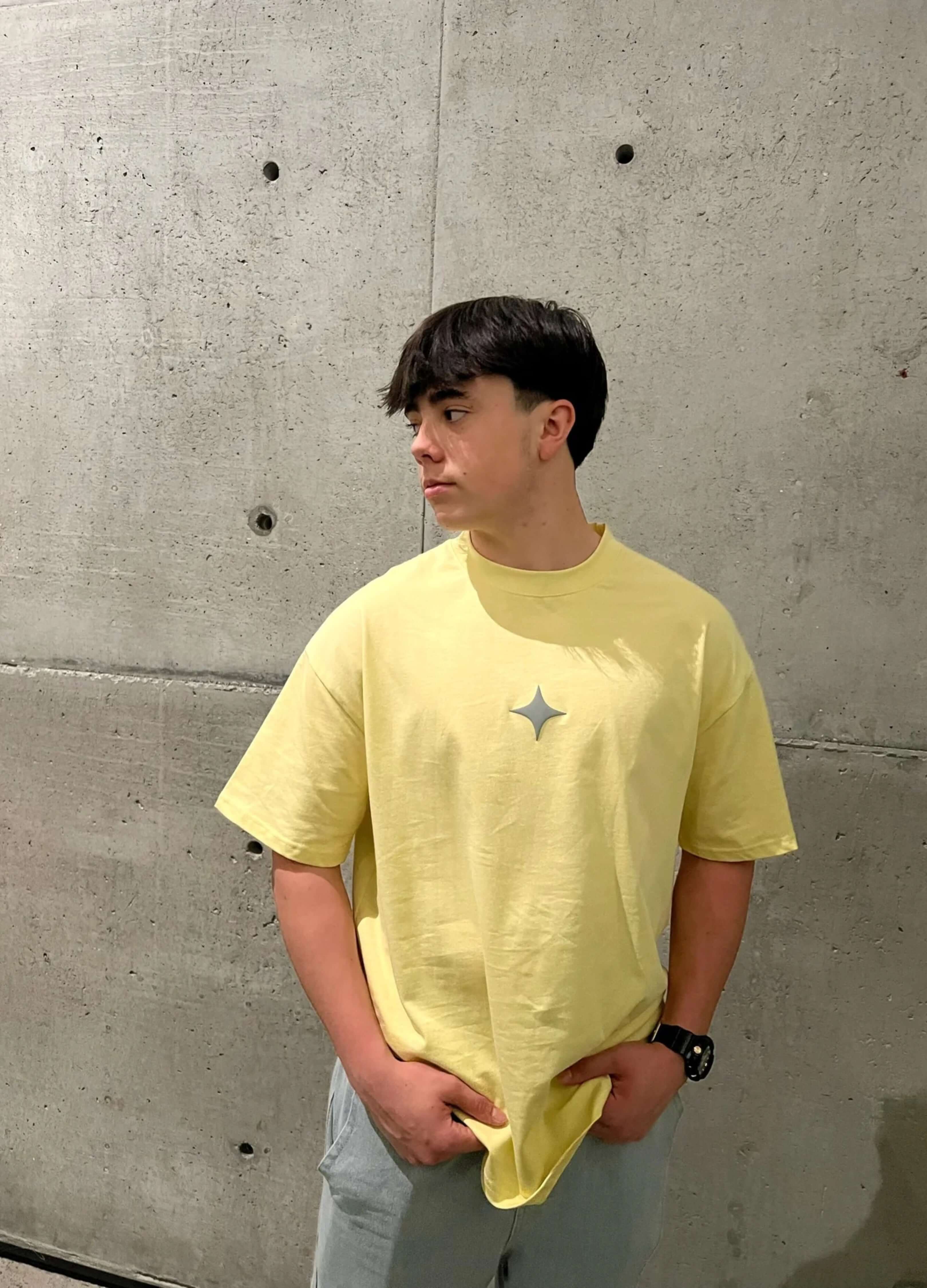 Young man wearing a yellow oversized tee with a chic grey print on a concrete background.