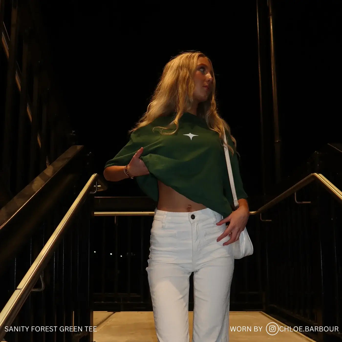 Woman wearing the Sanity Forest Tee in forest green with light blue print, styled with white pants for a chic look.