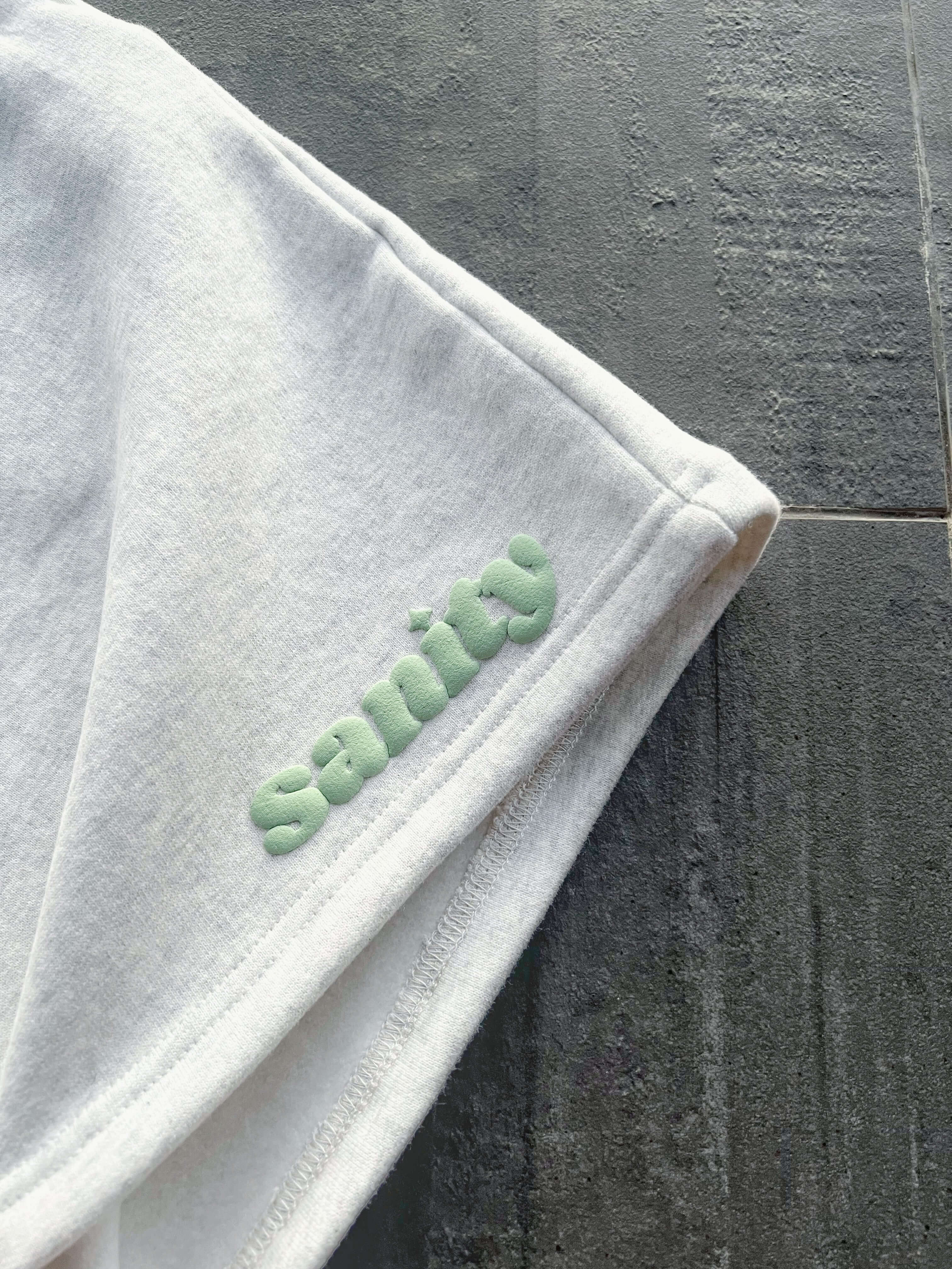 Close-up of white fabric showcasing the Sanity logo in green embroidery, emphasizing quality and style.
