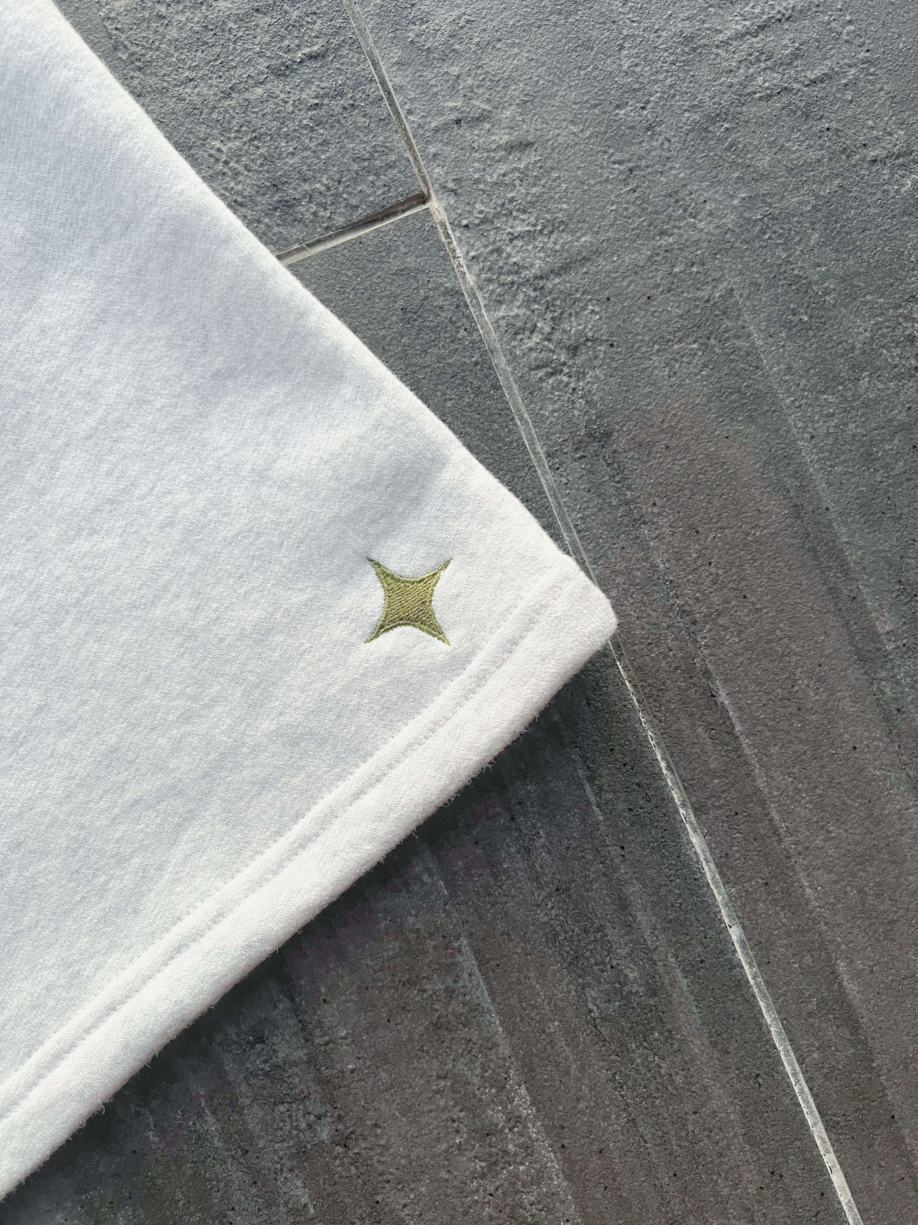 Close-up of the hem of Sanity Snow Men's Shorts featuring a green embroidered logo on white fabric.