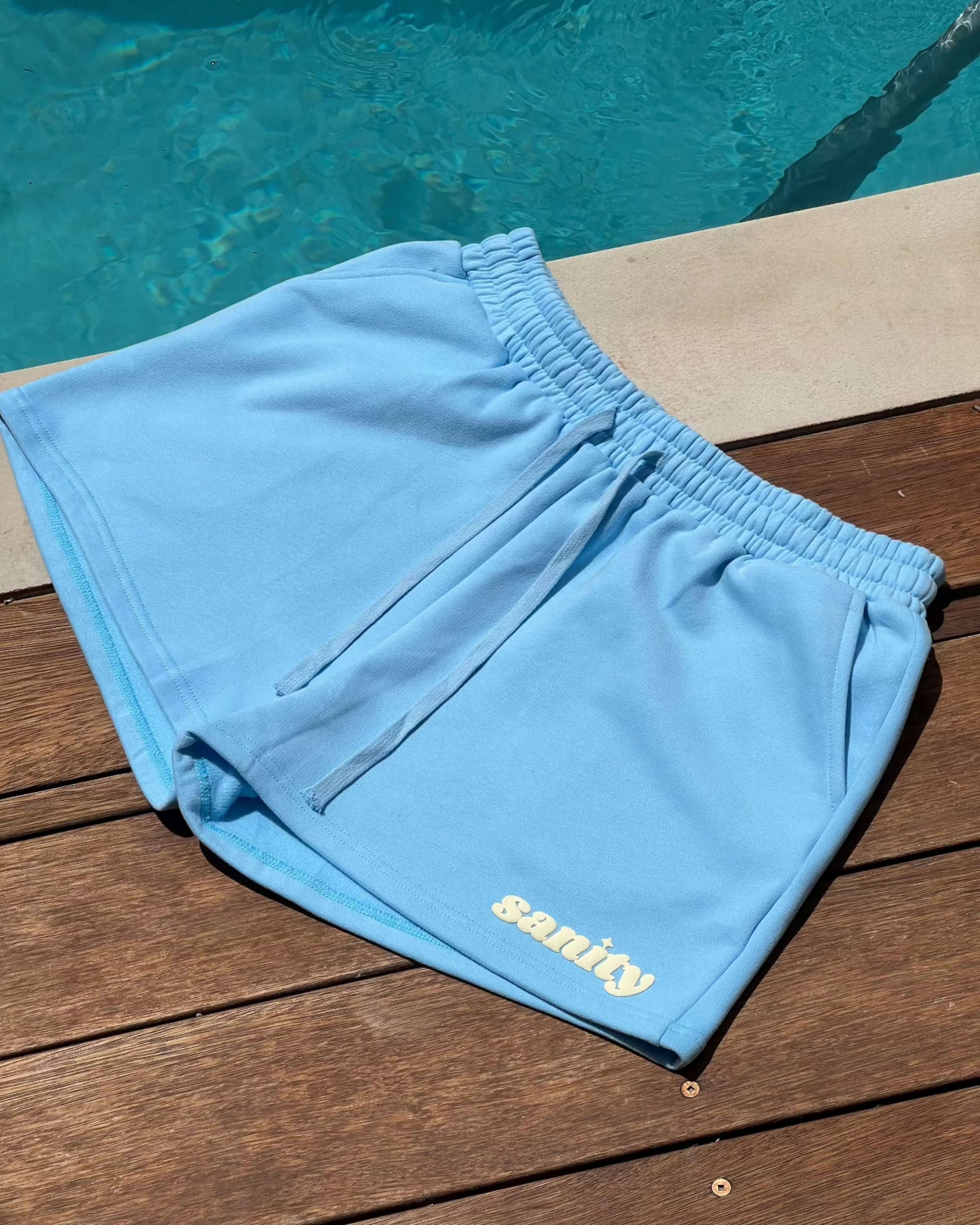 Sanity Ice Blue women's shorts on a wooden deck by the pool, showcasing a relaxed fit and comfort.