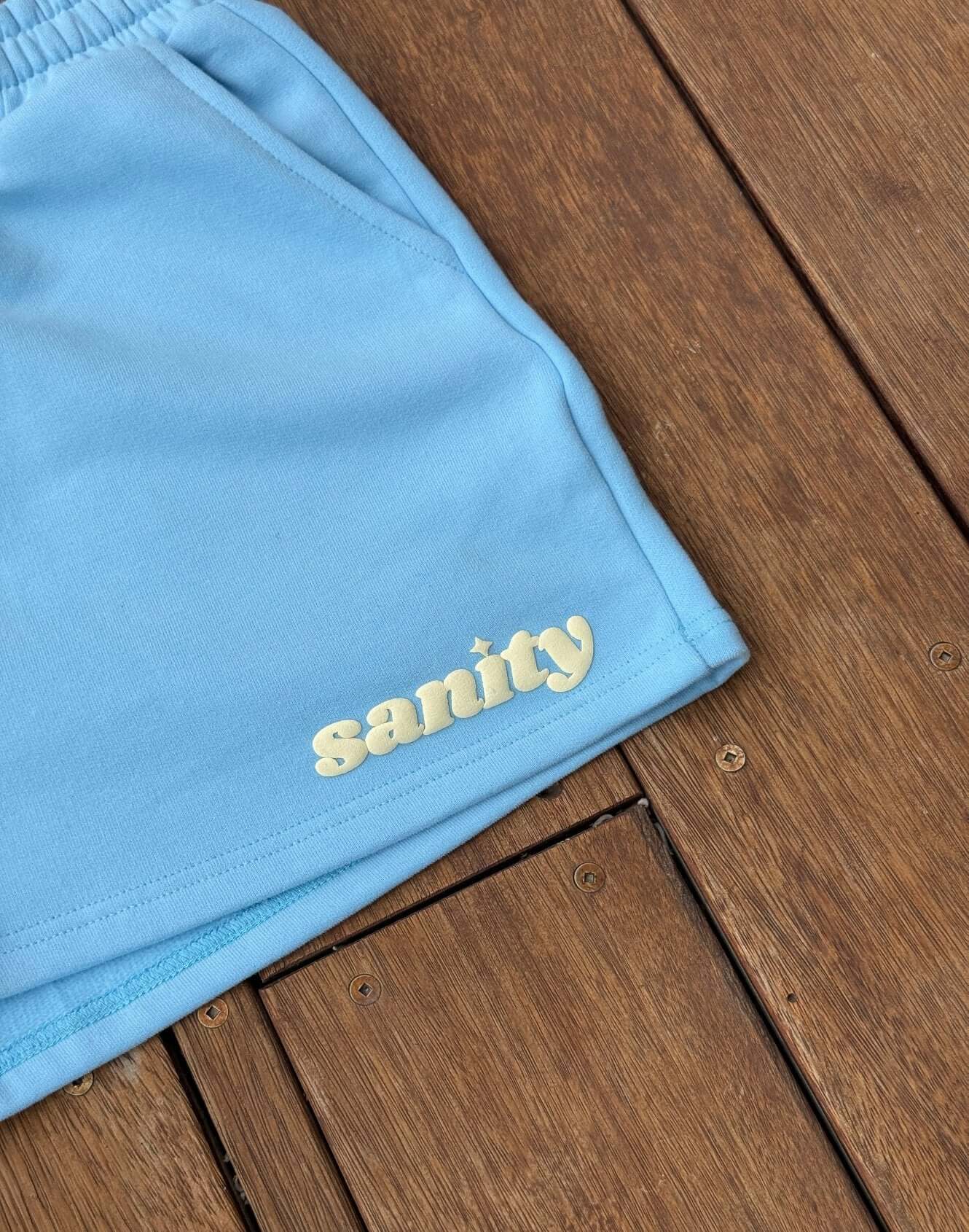Close-up of Sanity Ice Blue women's shorts showcasing logo and fabric on a wooden surface.