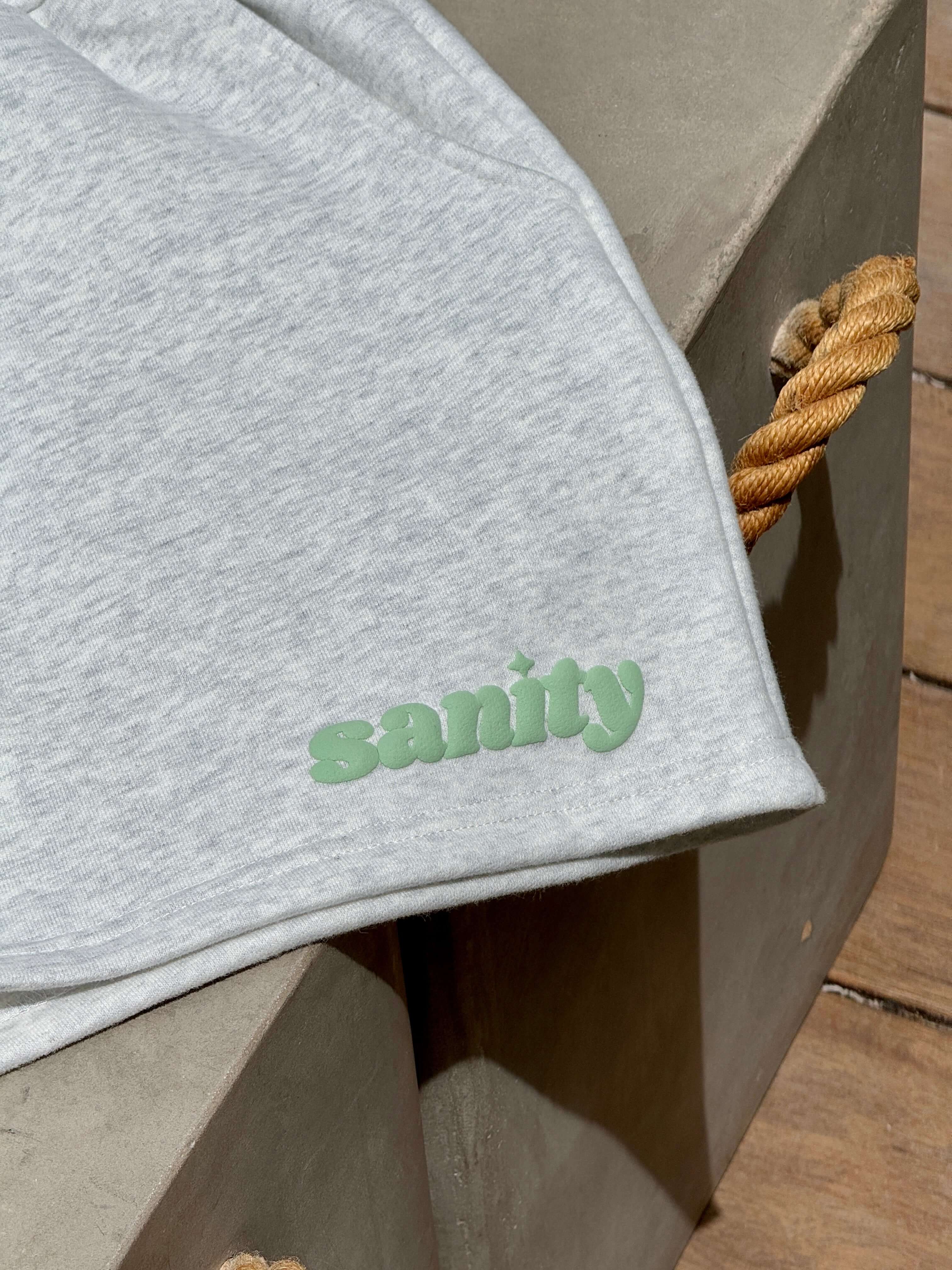 Close-up of Sanity brand logo on a light gray fabric, showcasing casual style and quality craftsmanship.