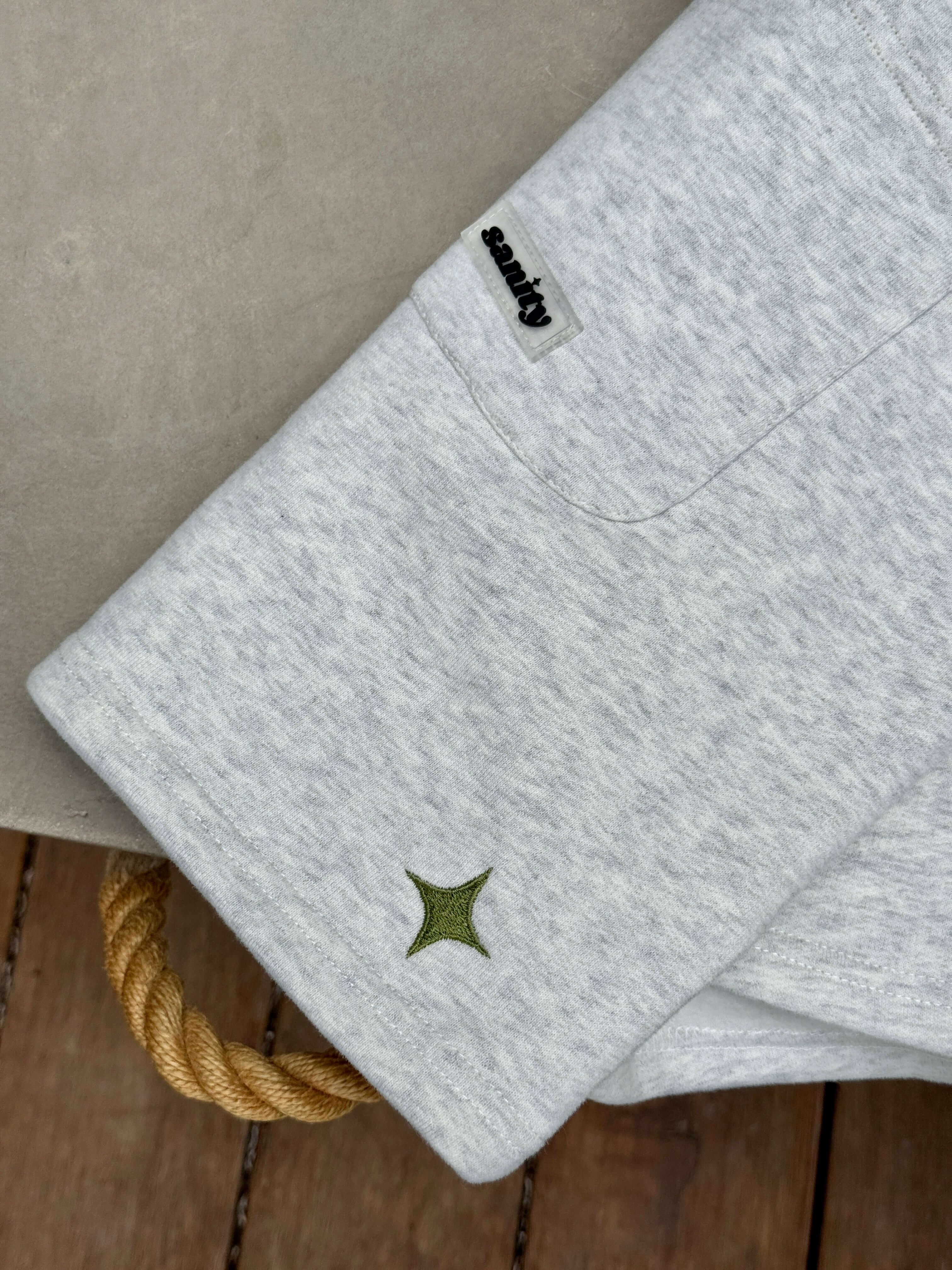 Close-up of Sanity brand logo and green emblem on grey fabric, showcasing casual style and quality craftsmanship.