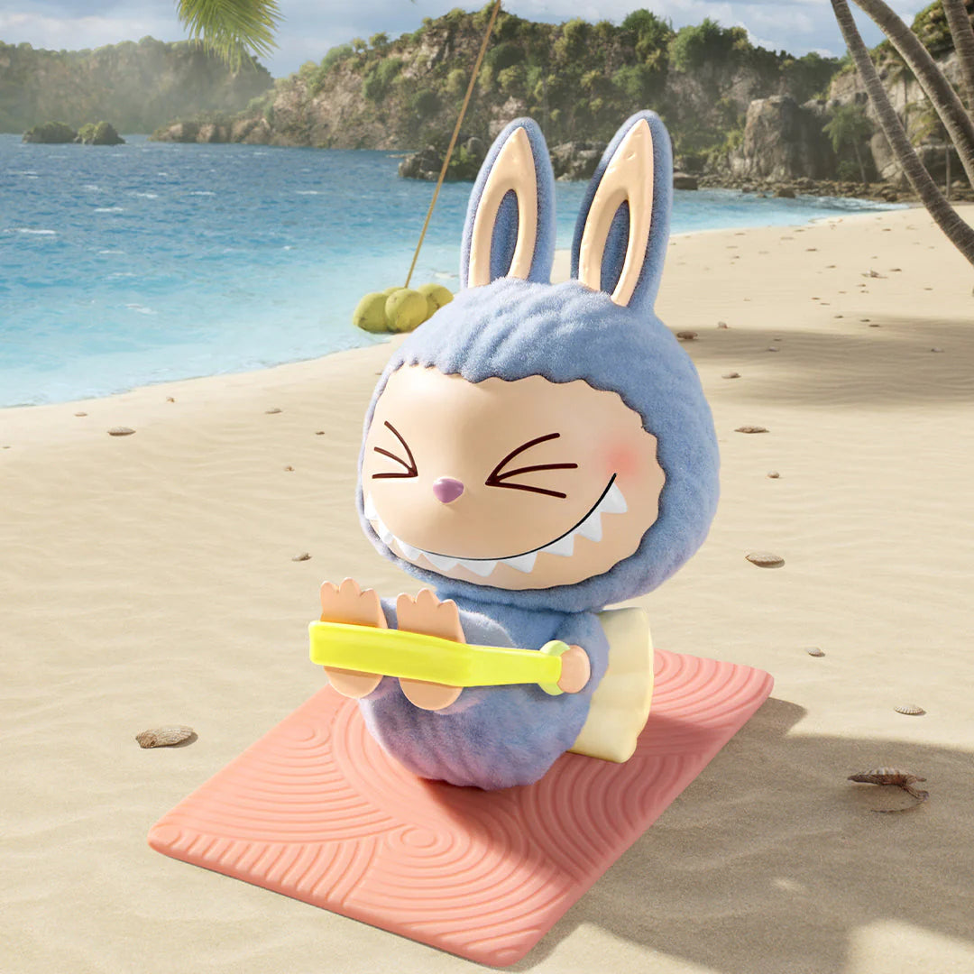 Pop Mart Labubu figure in a blue bunny costume practicing yoga on a beach mat by the ocean.