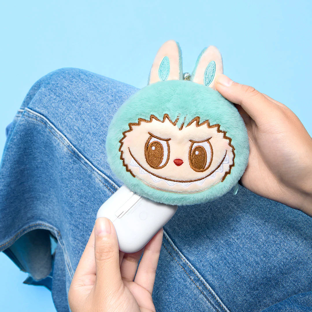 Person holding a mint green Labubu plush pouch with bunny ears, sitting on denim fabric.