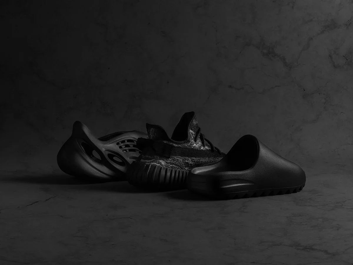 Three black Yeezy sneakers displayed artistically against a dark background.