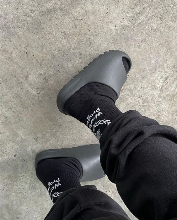 Person wearing Yeezy slide sandals with black socks, standing on a concrete surface.
