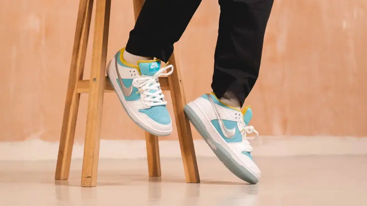 Close-up of a person wearing blue and white Nike Dunk sneakers while sitting on a wooden stool.